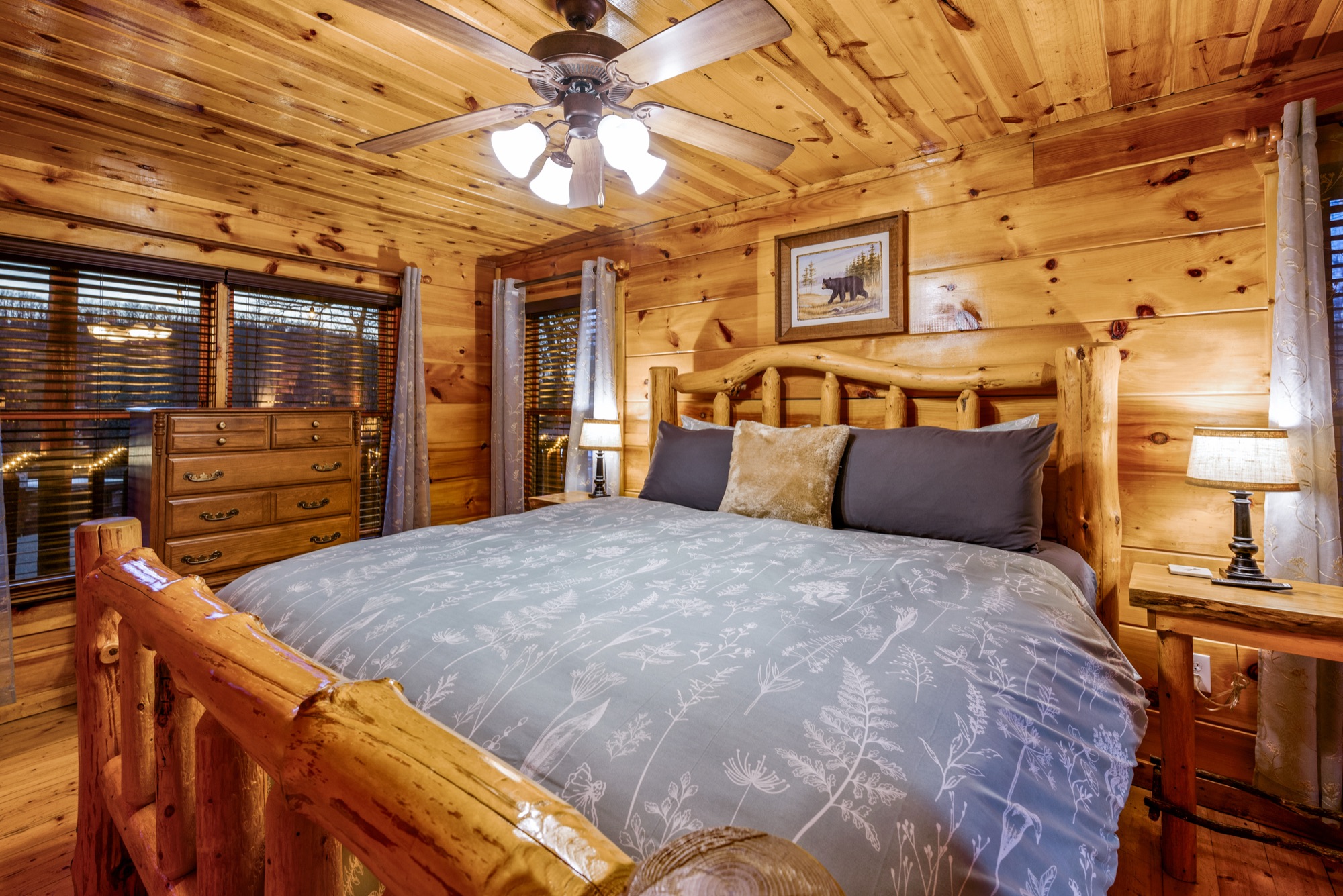 Primary bedroom at Bearadise with a king log bed in blue gray floral bedding, flanked by matching bedside lamps